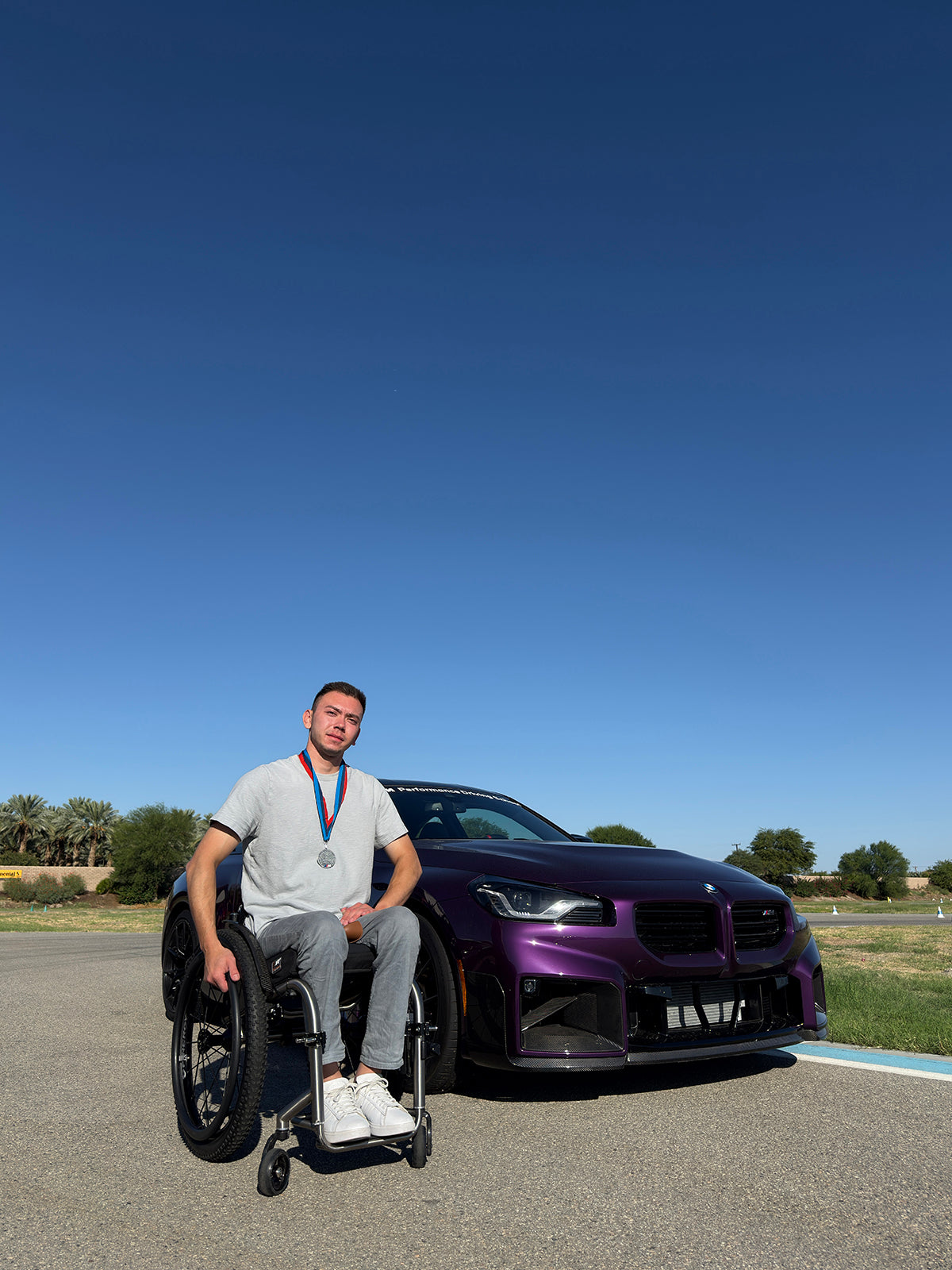 Darkhan in his wheelchair beside his purple BMW outdoors.